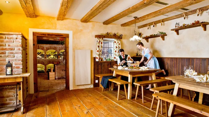 Rustikales bayerisches Restaurant mit Holzmöbeln, Serviererin in Dirndl deckt Tisch